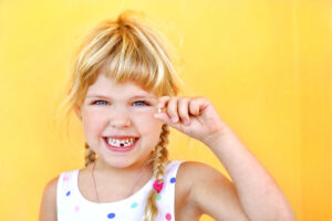 little girl smiling holding tooth